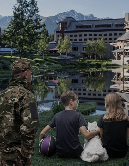 Children sitting at a hotel lake with a soldier looking on